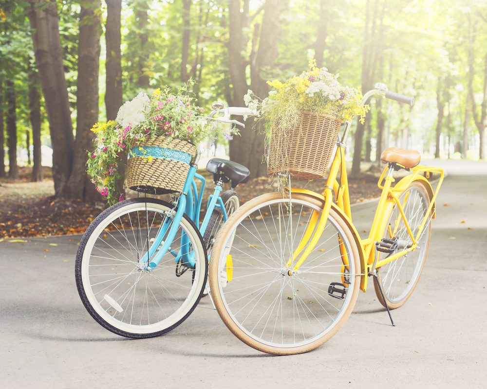 Yellow and turqoise city woman bicycles with flowers in park